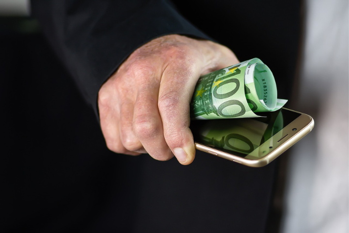 Hand, die Geld und Handy hält als Symbol für kostenpflichtige Features auf Social Media
